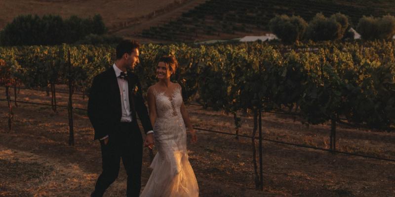 Couple walking through vineyard at sunset enjoying all inclusive wedding services at a scenic venue