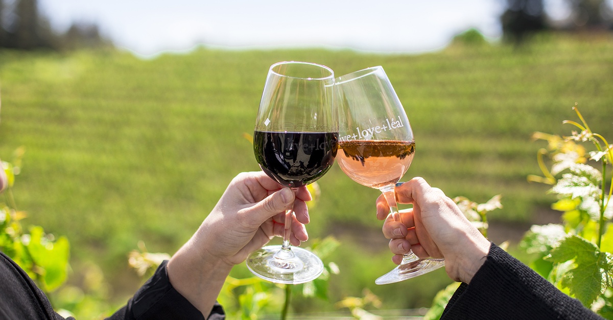 Couple clinking red and rosé wine glasses overlooking a California vineyard wedding destination