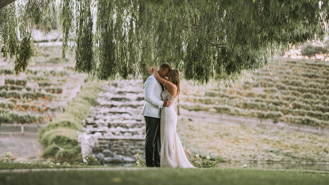 Couple embracing beneath willow trees at a vineyard, showcasing a seamless indoor-outdoor setting for private event venues.